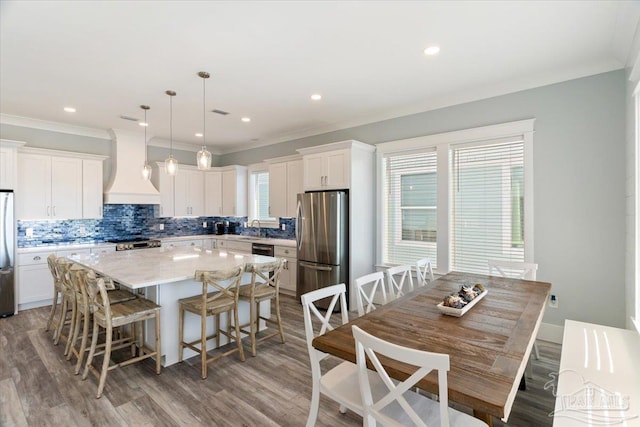 kitchen with white cabinetry, decorative light fixtures, a kitchen island, custom exhaust hood, and appliances with stainless steel finishes