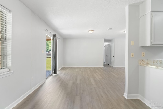 empty room with light wood-type flooring, baseboards, and a textured ceiling