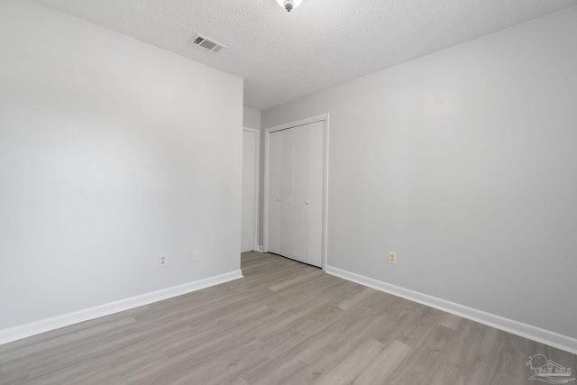 unfurnished room featuring a textured ceiling, light wood-style flooring, visible vents, and baseboards