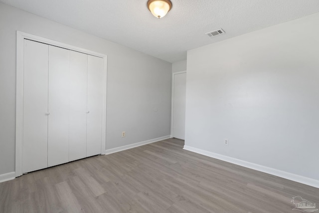 unfurnished bedroom featuring baseboards, wood finished floors, visible vents, and a closet