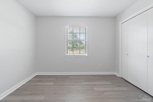 unfurnished bedroom with light wood-style flooring, a closet, and baseboards
