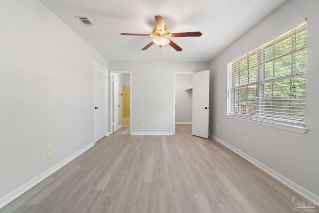 unfurnished bedroom with a textured ceiling, light wood-style flooring, visible vents, and a spacious closet