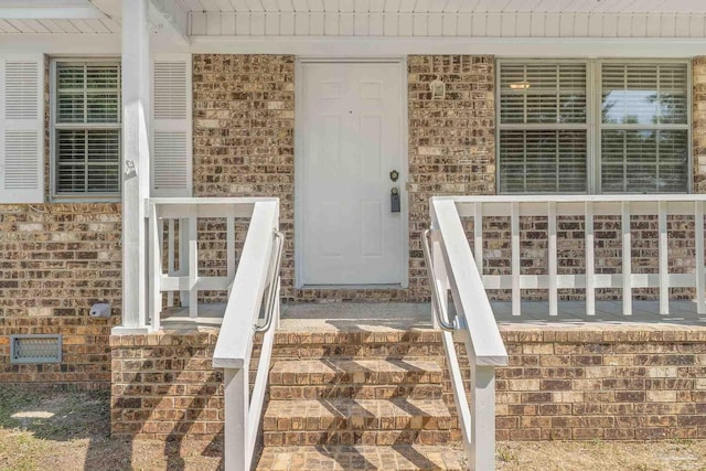 doorway to property featuring brick siding and covered porch