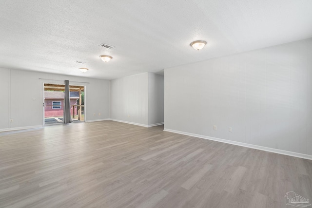 spare room featuring visible vents, light wood-style flooring, baseboards, and a textured ceiling