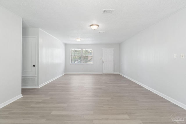 empty room featuring baseboards, a textured ceiling, visible vents, and light wood-type flooring