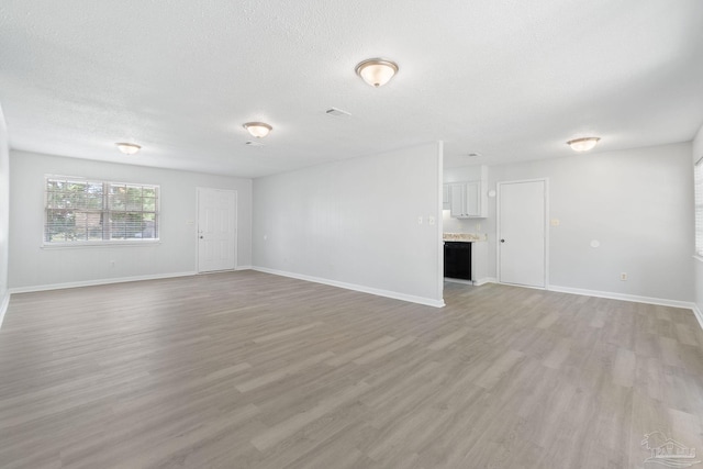 unfurnished living room with baseboards, a textured ceiling, and light wood finished floors