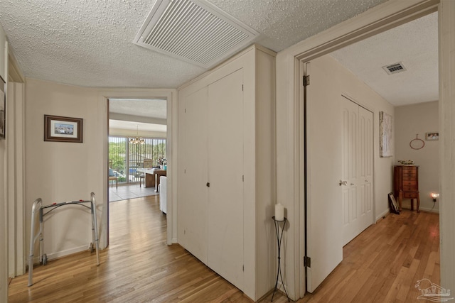 hall with a textured ceiling, light wood-style flooring, and visible vents