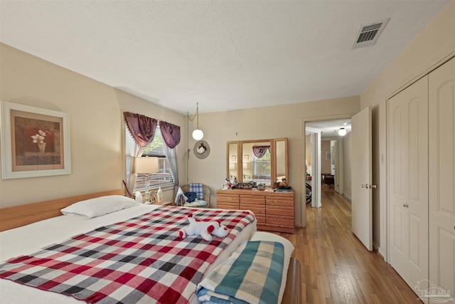 bedroom with hardwood / wood-style flooring, visible vents, a textured ceiling, and a closet