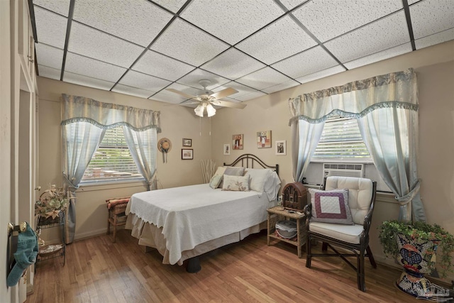 bedroom with hardwood / wood-style floors, cooling unit, ceiling fan, baseboards, and a paneled ceiling