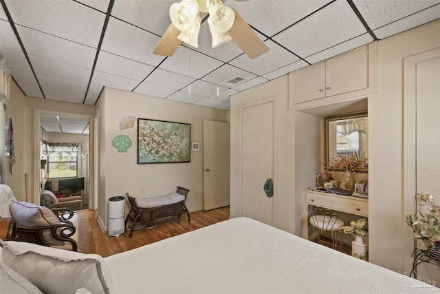 bedroom with wood finished floors, visible vents, ceiling fan, and a drop ceiling