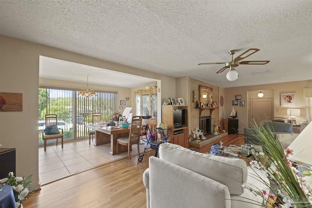 living area with ceiling fan with notable chandelier, a fireplace, a textured ceiling, and light wood finished floors
