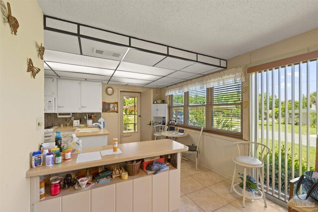 kitchen with white cabinets, visible vents, light tile patterned floors, a peninsula, and tasteful backsplash