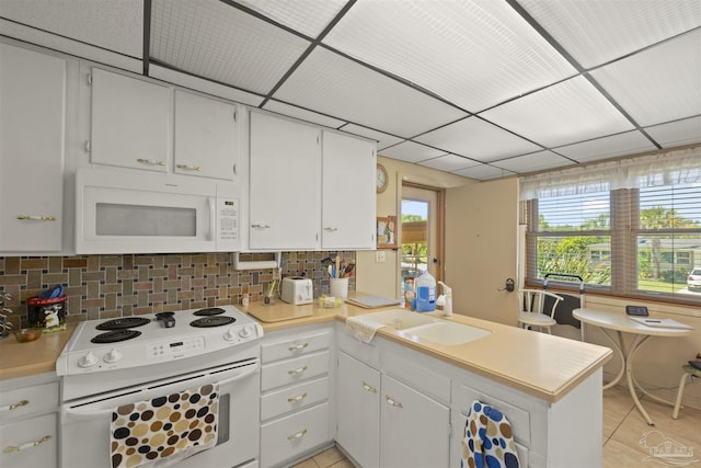 kitchen featuring a peninsula, a sink, white appliances, light countertops, and light tile patterned floors