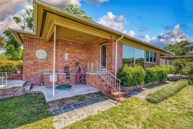 entrance to property featuring brick siding, a lawn, and a patio