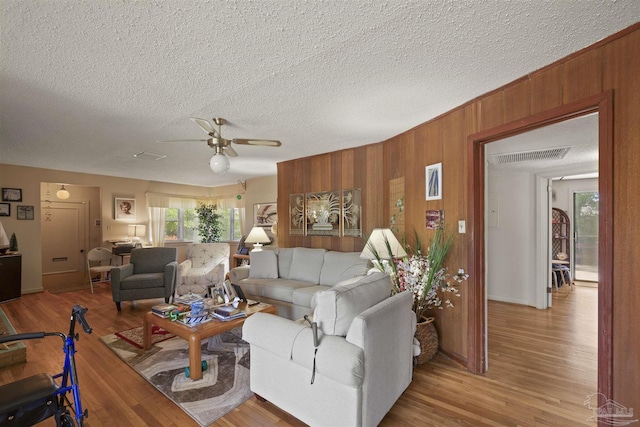 living area featuring wood walls, wood finished floors, visible vents, a ceiling fan, and a textured ceiling