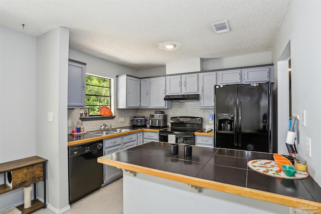 kitchen featuring a peninsula, a sink, visible vents, under cabinet range hood, and black appliances