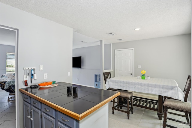 kitchen featuring a peninsula, a textured ceiling, visible vents, blue cabinetry, and tile counters