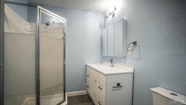 bathroom with vanity, a textured ceiling, a shower with door, hardwood / wood-style flooring, and toilet