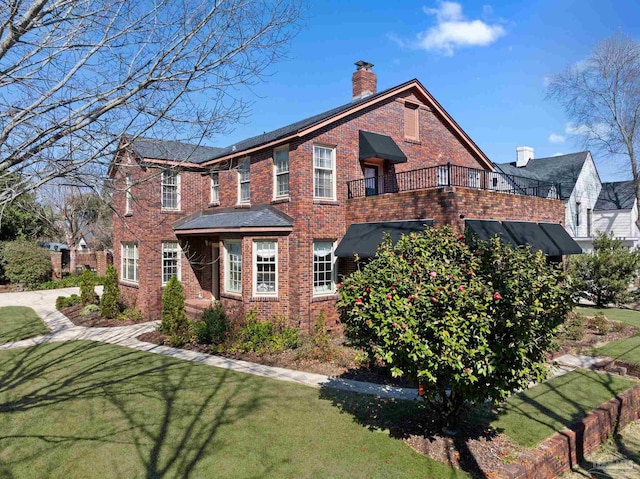 view of side of home with brick siding, a lawn, a chimney, and a balcony