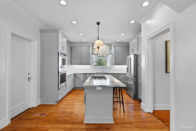 kitchen with a breakfast bar area, stainless steel appliances, gray cabinets, light wood-style floors, and light stone countertops