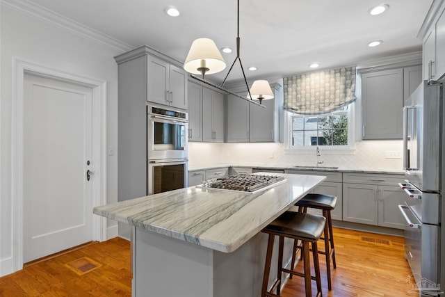 kitchen featuring a breakfast bar area, gray cabinetry, stainless steel appliances, a sink, and ornamental molding