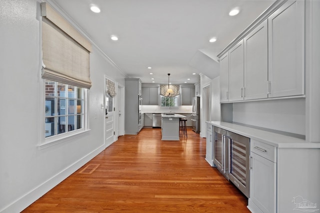 kitchen with beverage cooler, baseboards, a kitchen island, appliances with stainless steel finishes, and light wood-type flooring