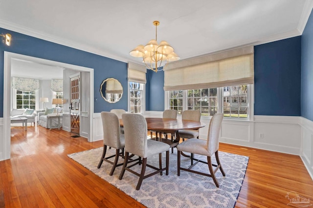 dining space featuring a chandelier, ornamental molding, a wainscoted wall, and wood finished floors