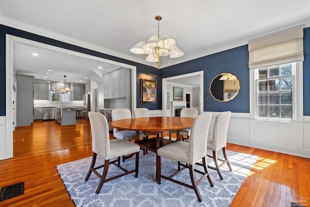 dining space with light wood finished floors, wainscoting, visible vents, and a notable chandelier