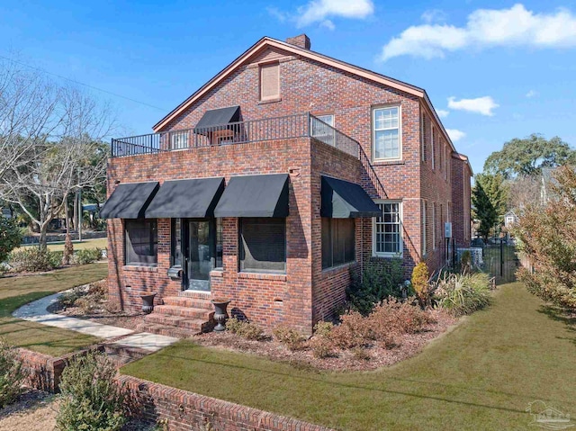 view of front of house featuring a balcony, a front lawn, and brick siding