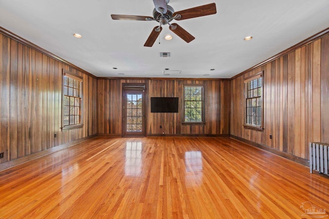 unfurnished living room with visible vents, ornamental molding, wood walls, light wood-type flooring, and baseboards