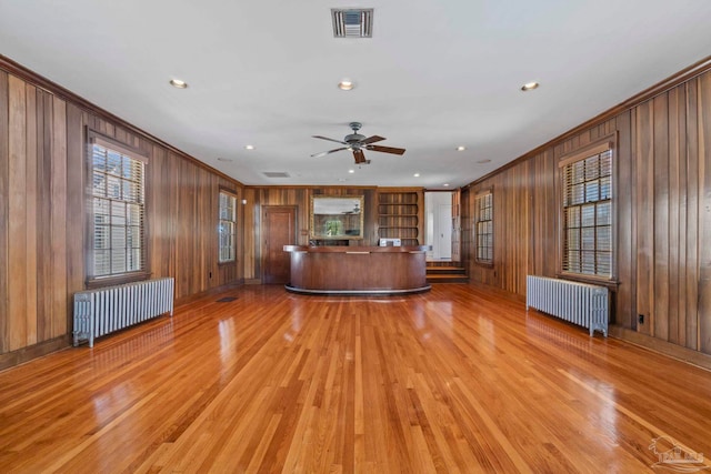 unfurnished living room featuring crown molding, wooden walls, visible vents, and radiator