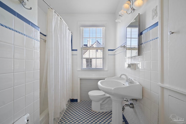 full bath with wainscoting, shower / bath combination with curtain, toilet, and tile walls