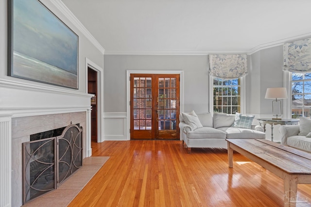 living room with french doors, crown molding, a fireplace, light wood-style flooring, and wainscoting