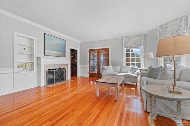 living room with built in shelves, french doors, light wood-style floors, and a fireplace with flush hearth