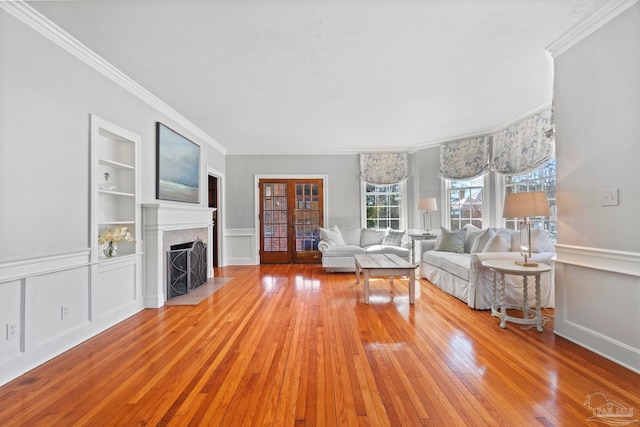 unfurnished living room featuring built in shelves, a wainscoted wall, a fireplace with flush hearth, ornamental molding, and wood-type flooring