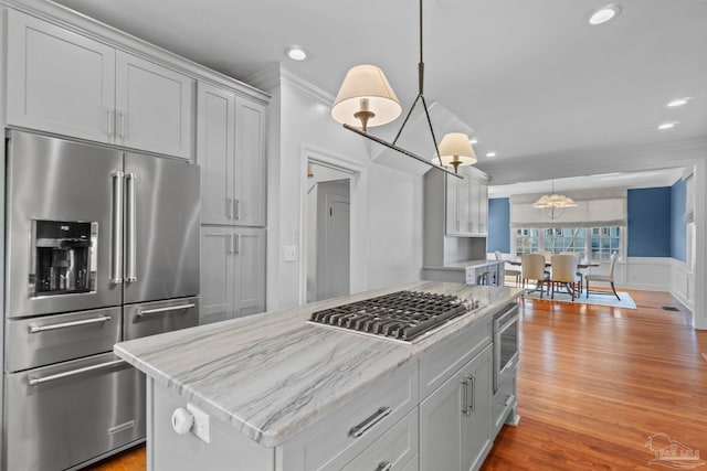 kitchen with stainless steel appliances, wood finished floors, a center island, and crown molding