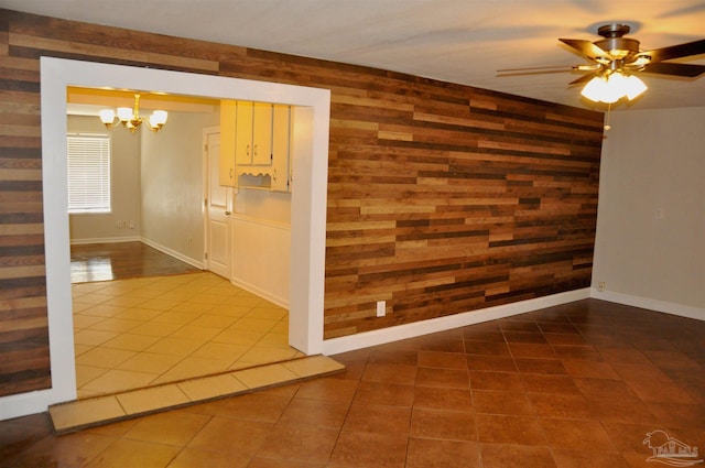 tiled empty room with baseboards, wooden walls, and ceiling fan with notable chandelier