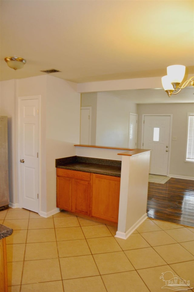 kitchen featuring light tile patterned floors, dark countertops, a chandelier, and brown cabinetry