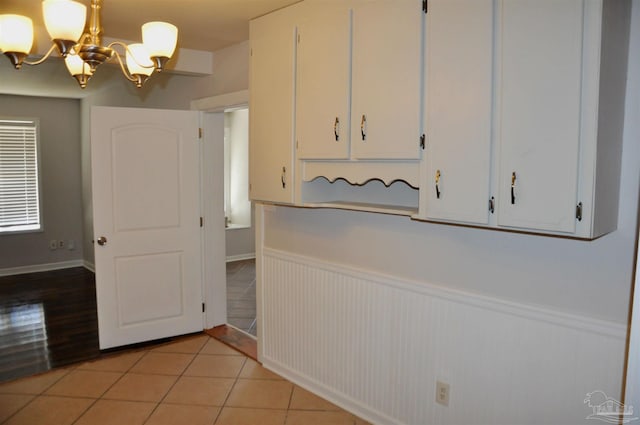 interior space with a chandelier, light tile patterned floors, wainscoting, and white cabinetry