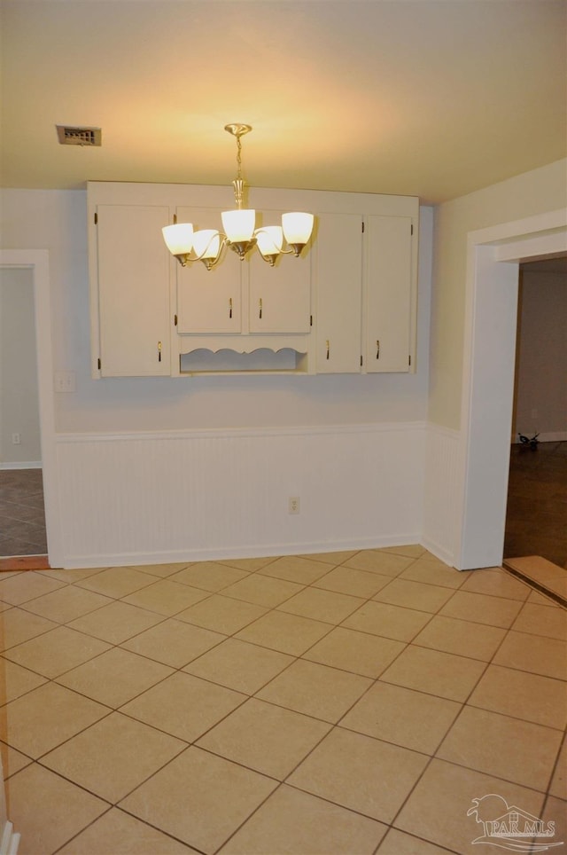 unfurnished room featuring light tile patterned floors, a notable chandelier, wainscoting, and visible vents