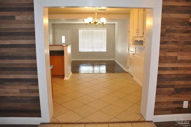 doorway featuring light tile patterned floors, wooden walls, visible vents, and an inviting chandelier