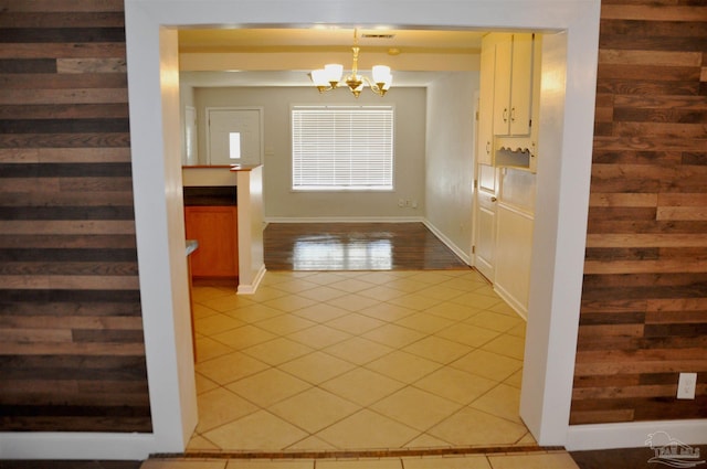 doorway with an inviting chandelier, light tile patterned flooring, visible vents, and wood walls