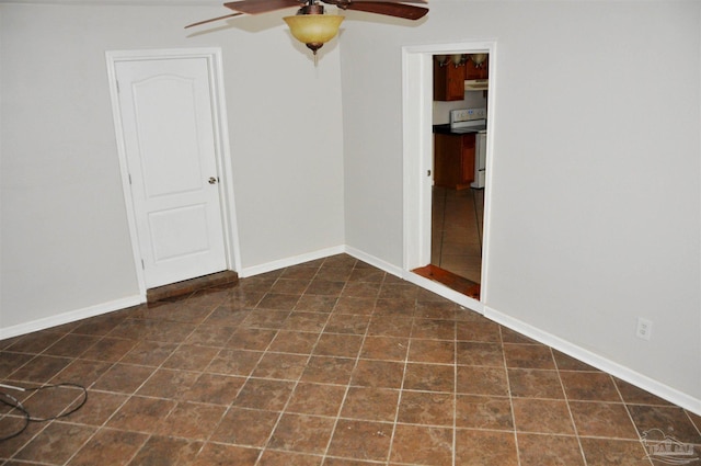 unfurnished room with dark tile patterned floors, ceiling fan, and baseboards