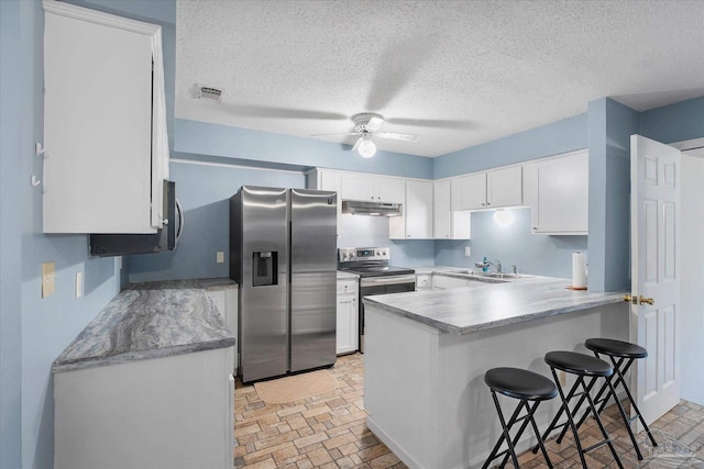 kitchen featuring ceiling fan, appliances with stainless steel finishes, a kitchen breakfast bar, and white cabinetry