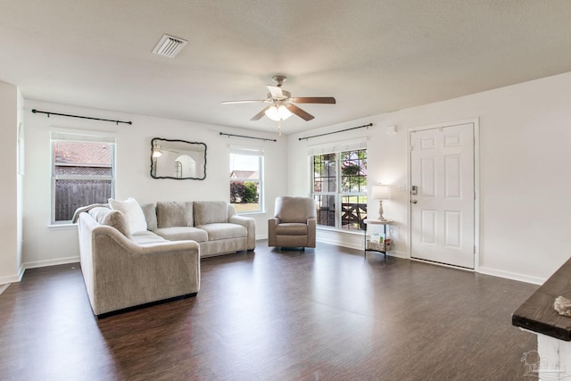 living room featuring visible vents, a ceiling fan, baseboards, and dark wood-type flooring