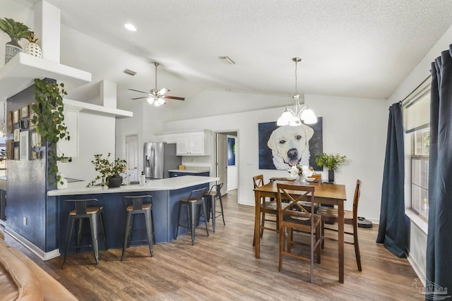 interior space with stainless steel refrigerator with ice dispenser, hanging light fixtures, dark hardwood / wood-style floors, a kitchen bar, and white cabinetry