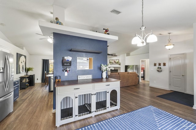 kitchen featuring ceiling fan with notable chandelier, vaulted ceiling, stainless steel fridge, decorative light fixtures, and dark hardwood / wood-style flooring