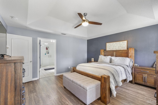 bedroom featuring hardwood / wood-style flooring, ceiling fan, a raised ceiling, and connected bathroom