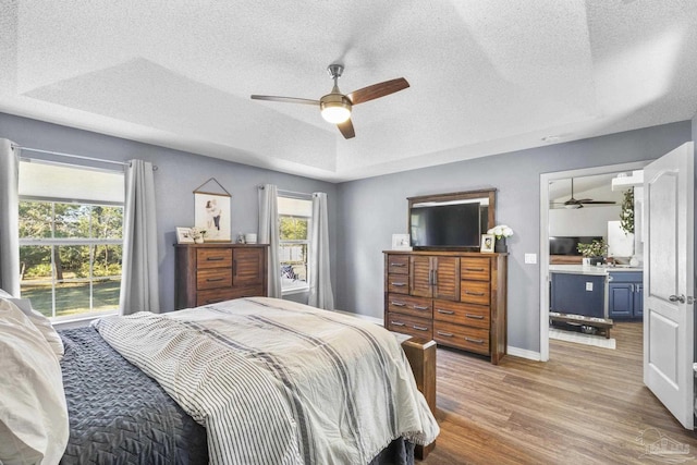 bedroom featuring light wood-type flooring, a raised ceiling, and ceiling fan