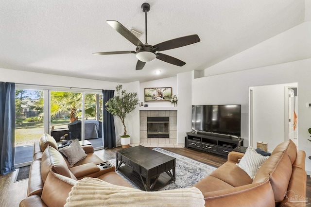 living room with a textured ceiling, ceiling fan, a tile fireplace, hardwood / wood-style flooring, and lofted ceiling